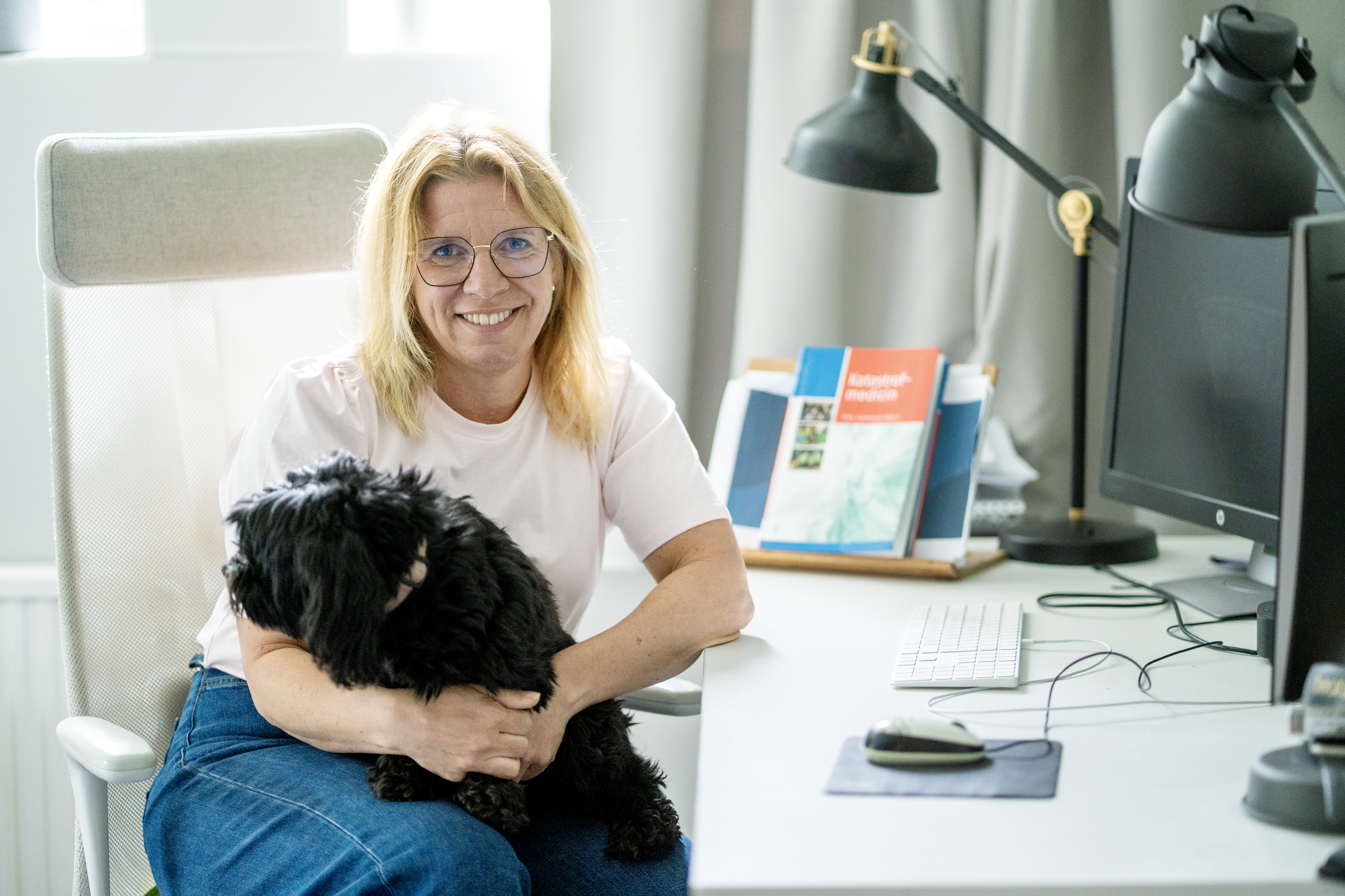 Kvinna sitter vid skrivbord med en svart hund i sitt knä.