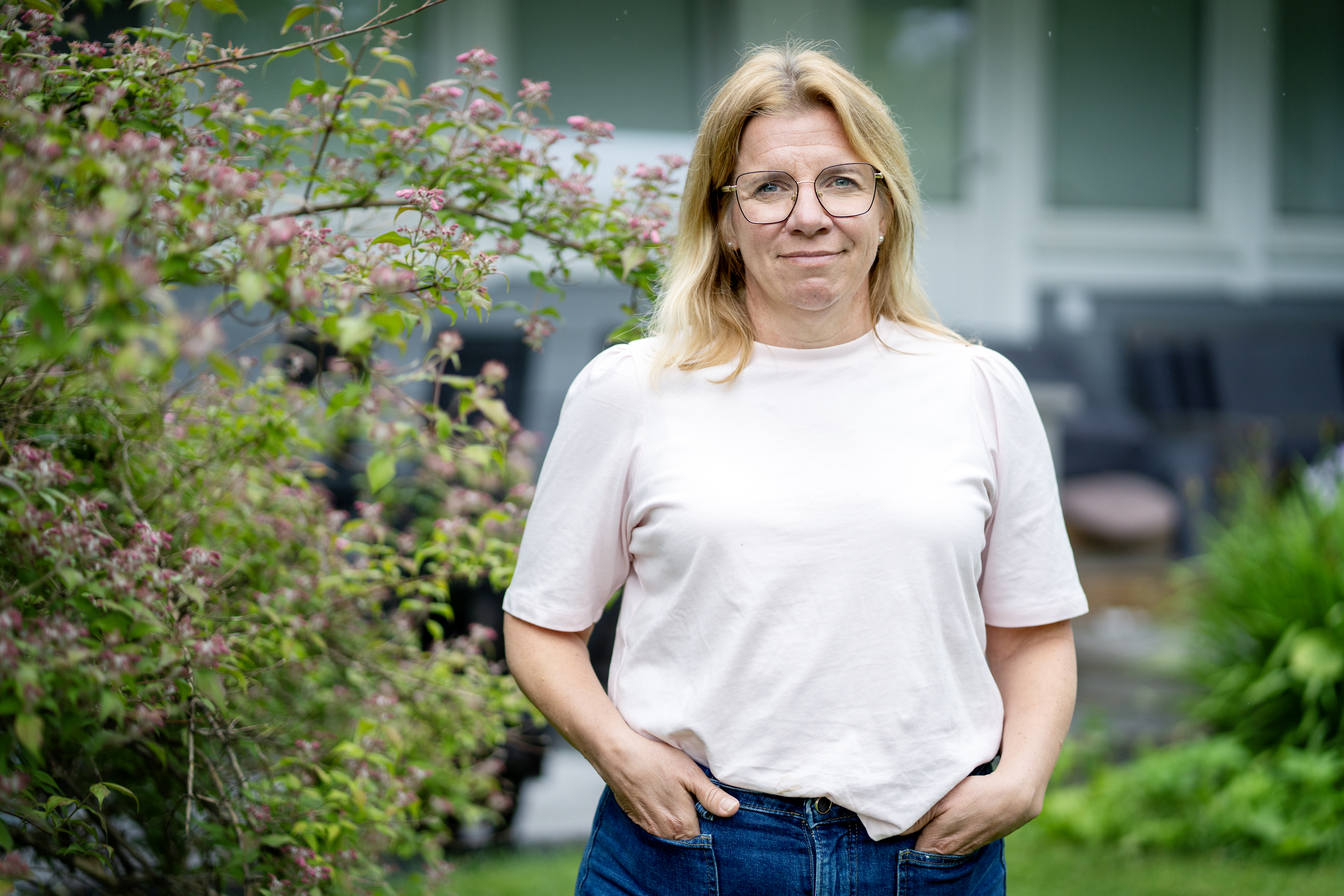 Kvinna i vit t-shirt och blå jeans står med händer i byxfickor.