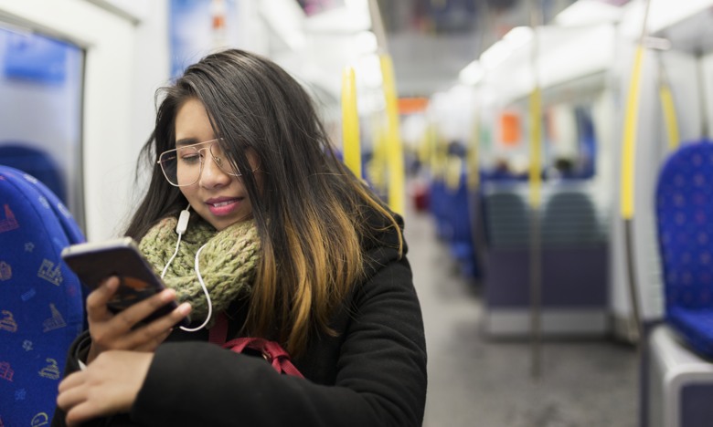 Ungkvinna sitter på tunnelbanetåg och tittar i mobilen