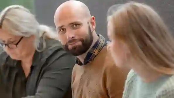 En man sitter mellan två kvinnor och tittar in i kameran. 