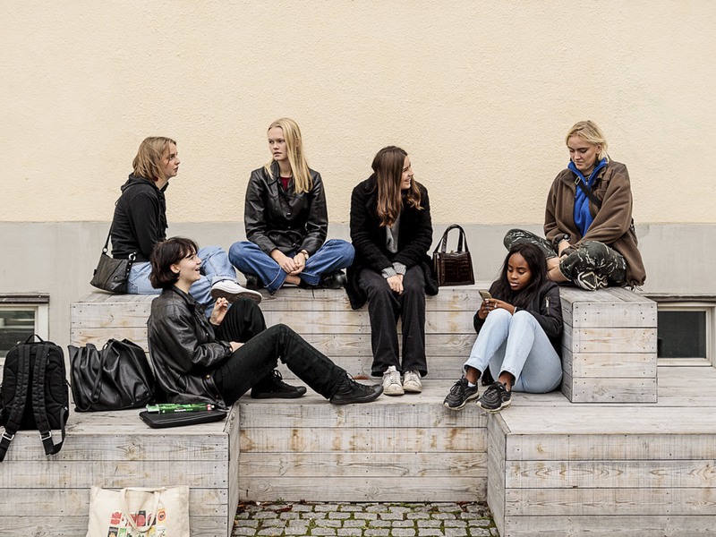 Ett gäng tjejer i gymnasieålder sitter utanför en skola under en rast. 