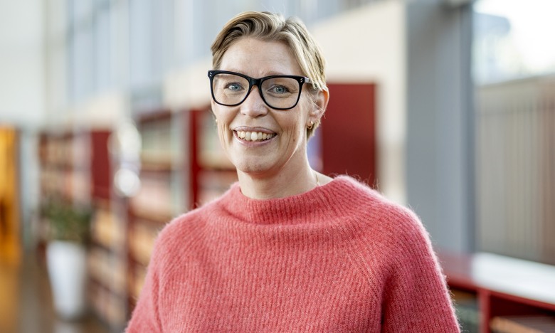 Therese har rosa tröja på sig och står i en korridor i kontorsmiljö.