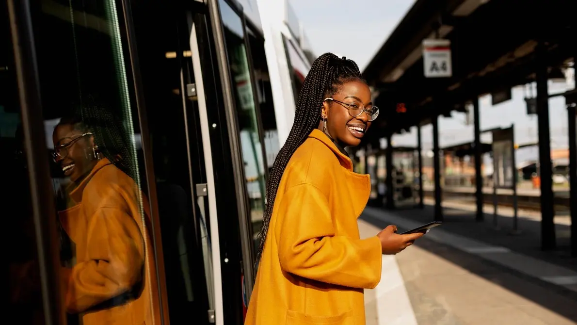 Glad kvinna kliver av ett tåg och har en mobil i sin hand.